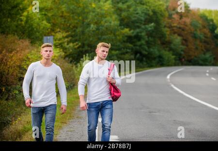 Touristenreisende fahren mit Auto. Probleme beim Transport. Stelle auswählen, an der das Auto leicht zur Seite ziehen kann. Männer Rucksack Laufstraße. Zwillinge gehen auf der Straße. Abenteuerkonzept. Jungs hitchwander auf der Straße. Stockfoto