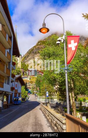 Zermatt, Schweiz - 7. Oktober 2019: Blick auf die Straße der Stadt mit Kirche in berühmtem Skigebiet und schweizer Flagge Stockfoto