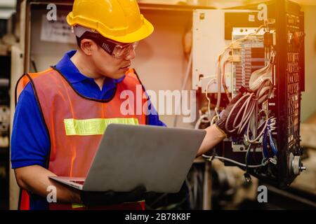 Servicetechniker-Team, das mit der elektronischen Drahtrückseite der Schwerindustriemaschine für die Reparatur von Wartungsarbeiten arbeitet und mit einem Laptop-Computer für Analys repariert Stockfoto