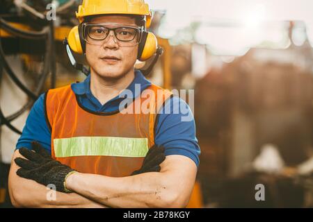 Asiatischer Techniker, der Ohrmuscheln trägt, schützt vor Lärm und Sicherheitsanzug, der im Portrait des Werks verwendet wird. Stockfoto