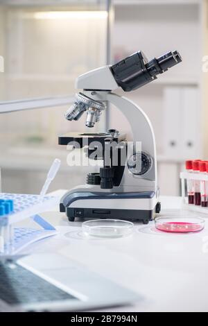 Mikroskop von Wissenschaftler oder Biologen, Petrischalen und Kolben am Arbeitsplatz im chemischen Labor mit niemandem in der Nähe Stockfoto