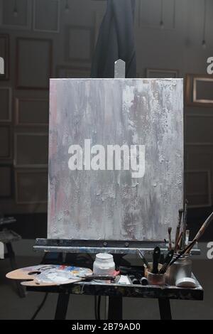 Staffelei mit unfertigen Bildern und einem Set von Materialien für professionelle Malerei im Klassenzimmer moderner Kunstschulen oder Studios Stockfoto
