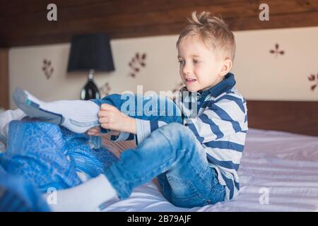 Fünf Jahre alter Junge kleidet morgens seine Socken auf dem Bett Stockfoto