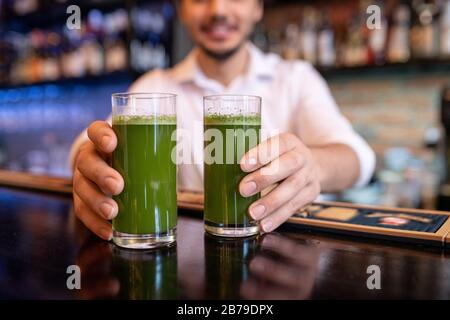 Hände junger Kellner oder Barmann, die zwei Gläser grünen Gemüsecocktail auf die Theke legen, während sie die Gäste des Cafés bedienen Stockfoto