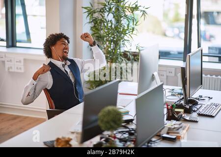 Fröhlicher afroamerikanischer Geschäftsmann, der Musik in Kopfhörern bei der Arbeit hört Stockfoto