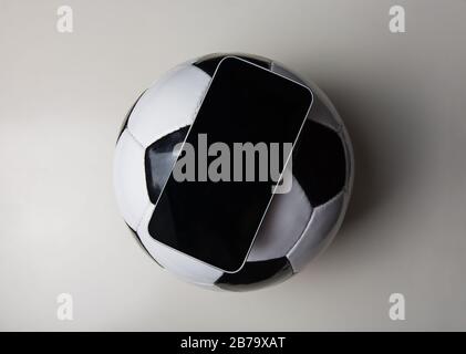 Live-Fußball-Wettkonzept, Online-Übertragung, leerer Smartphone-Bildschirm über einem klassischen Fußball isoliert auf weißem Hintergrund. Sportspiele winn Stockfoto