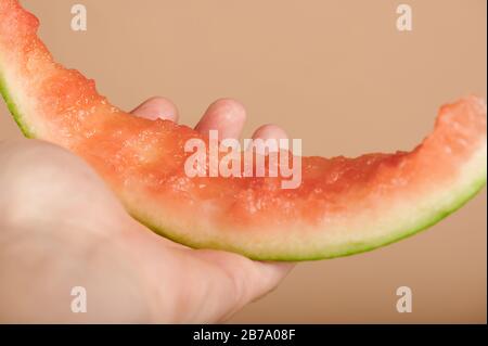 Halten Sie die verzehrte Wassermelonenscheibe in Nahaufnahme auf beigefarbenem Farbhintergrund Stockfoto