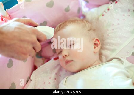 Messung der Temperatur kleiner Kinder mit kontaktlosem Thermometer. Infrarot-Thermometer in den Händen der Mutter. Stockfoto