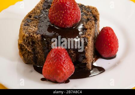 Zwei Schokoladenkuchen mit mehreren Erdbeeren oben in schwarzer Platte auf gelbem Tischhintergrund Stockfoto