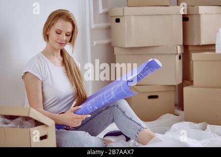 Mädchen sitzt zwischen Boxen macht Marken auf dem Plan der Wohnung Stockfoto