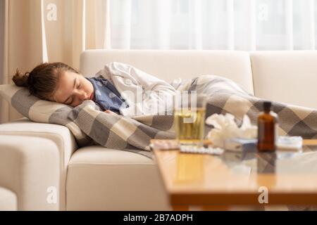 Schlafendes junges krankes Mädchen, das auf einem Sofa mit kaltem und hohem Fieber liegt. Stockfoto