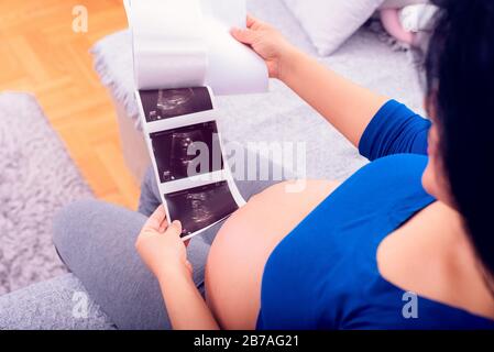 Schwangere Frau, die den Ultraschalldruck ihres ungeborenen Babys betrachtet. Stockfoto