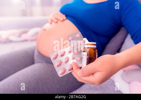 Vitamine während der Schwangerschaft. Schwangere Frau, die Pillen in der Hand hält und ihren Bauch aussetzt. Stockfoto