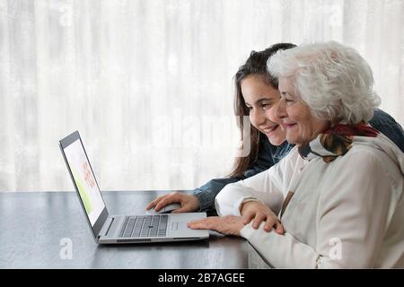 Die Enkelin, die ihrer Großmutter beigebracht hat, einen Computer auf einem Holztisch mit einem bunten Taschentuch zu benutzen, das Konzept der Liebe, Freundschaft, Technologie, Heilung Stockfoto