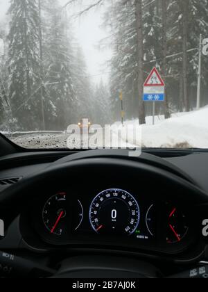 Das Fahren unter schwierigen Straßenbedingungen am nebligen Tag in italienischen Bergen aus Sicht des Fahrers, einschließlich Tacho, Straßen- und Schneefräse Stockfoto