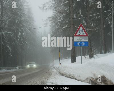 Foggy Day auf den straßen der italienischen alpen und eisiges Straßenschild und ein Auto im Hintergrund Stockfoto