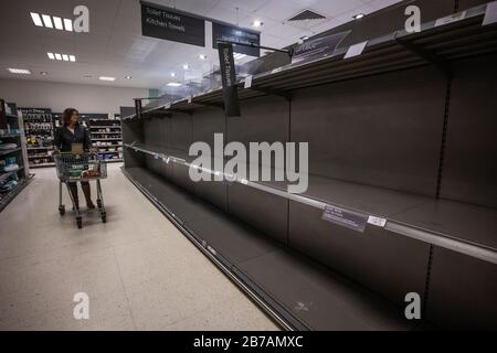 Eine Familie läuft nach dem Panikkauf von toilettenrollen durch das vereinigte Königreich wegen des Ausbruchs von Coronavirus an einem leeren Supermarktgang entlang. Stockfoto