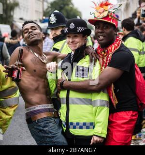 Zwei Enthüller posieren für ein frech Foto mit einem Polizisten im Nottinghill Carnival in London. Stockfoto