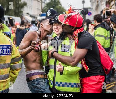 Zwei Enthüller Pflanzen einen frechen Kuss auf einen Polizisten, als sie den Daumen nach oben auf dem Nottinghill Carnival in London gibt. Stockfoto