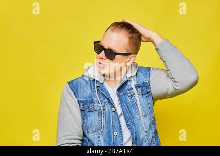Stilvoller kaukasischer Mann in einer Jeans und Sonnenbrille auf gelbem Hintergrund glättet seine Haare. Nahaufnahme. Stockfoto