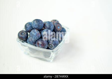 Blaubeeren in einem Glasbecher auf weißem Holzhintergrund. Nahaufnahme. Stockfoto