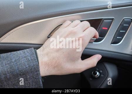 Ein Mann in einem modernen Auto. Die Hand zieht den Hebel, um die Tür zu öffnen. Nahaufnahme. Stockfoto