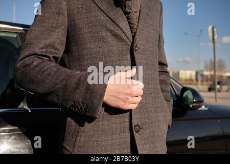 Ein Mann in einem Mantel ist unverfastet, eine Hand steht in der Nähe des Autos. Nahaufnahme. Stockfoto