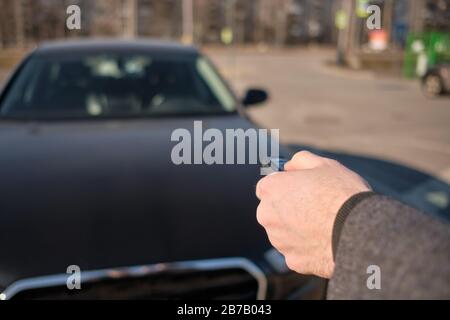 Der Mann im Mantel schickte die Schlüsselkette zum Auto, um den Alarm einzuschalten. Nahaufnahme. Stockfoto