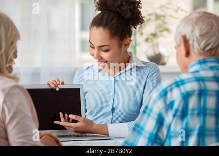 Afrikanische Abstiegsfrau Reisebüro im Büro lächelnd glücklich, Firmenwebsite auf Laptop zu ältern Paar zurück Ansicht Nahaufnahme zu zeigen Stockfoto