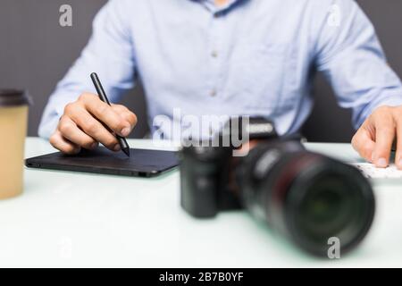 Hände nah oben, Seitenansicht. Die Arbeit eines Grafikdesigners. Fotoausrüstung auf dem Tisch. Retuschieren von Fotos Stockfoto