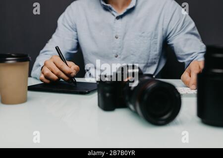 Hände nah oben, Seitenansicht. Die Arbeit eines Grafikdesigners. Fotoausrüstung auf dem Tisch. Retuschieren von Fotos Stockfoto