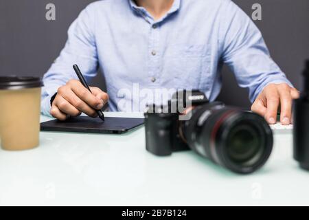 Hände nah oben, Seitenansicht. Die Arbeit eines Grafikdesigners. Fotoausrüstung auf dem Tisch. Retuschieren von Fotos Stockfoto