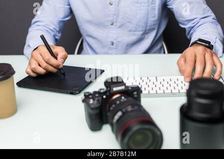 Hände nah oben, Seitenansicht. Die Arbeit eines Grafikdesigners. Fotoausrüstung auf dem Tisch. Retuschieren von Fotos Stockfoto