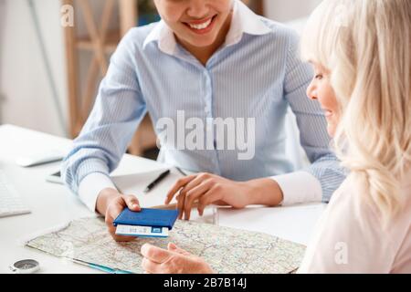 Afrikanischer Absteiger, weiblicher Reisevermittler im Büro, der Reisepass und Flugticket an eine ältere Frau gibt, die positiv lächelt und einen Service in der Nähe bietet Stockfoto