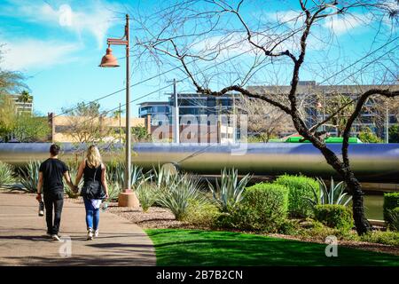 Rückansicht des jungen Paares auf einem Gehweg rund um die AZ-Kanalufer gegenüber der Paolo Soleri Brücke und der plaza in Scottsdale, AZ, USA Stockfoto