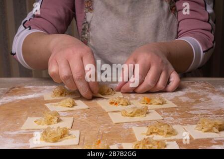 Eine Frau sculpt Knödel und Ravioli aus Kneten und Kohl. Sperrholzschneidplatte, Holzmehlsieb und Walzstift aus Holz - Werkzeuge für Stockfoto
