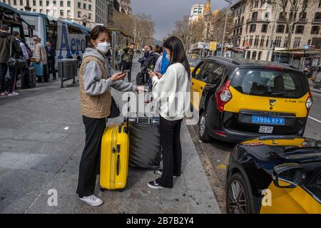 Zwei asiatische Touristen, die Gesichtsmasken als Vorsichtsmaßnahme gegen die Verbreitung von Coronavirus tragen, warten auf den Aerobus, der für den Flughafen Barcelona gebunden ist.Nachdem die spanische Regierung den "Alarmzustand" angeordnet hat, bleiben nur noch Grundeinrichtungen wie Supermärkte, Apotheken und Tabakhändler in Barcelona geöffnet. Stockfoto