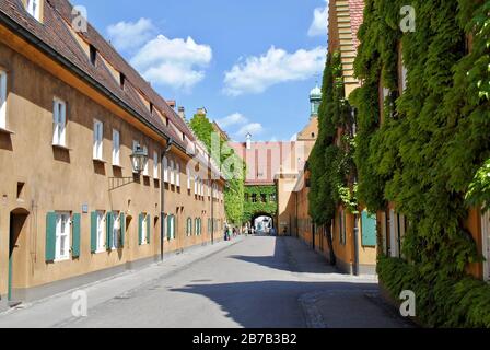 Augsburg: Senfgelbe Wände und grüne verschlafene Fenster der Fuggerei. Die Fuggerei ist der älteste soziale Wohnkomplex der Welt. Stockfoto