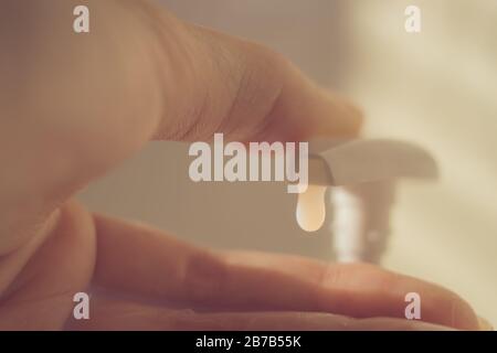 Fingerberührung mit einer Flüssigseifenspender. Weißes Gel fällt aus der Flasche. Stockfoto