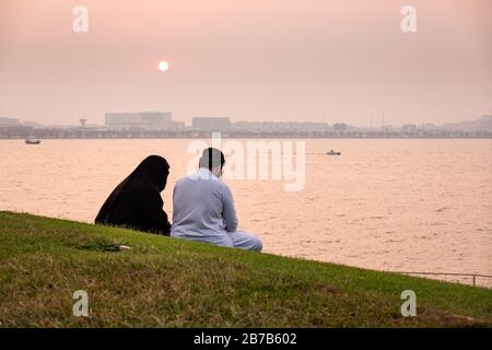 Ein muslimischer Mann und eine Frau in einer Burka und Taube beobachten den Sonnenuntergang über dem Hafen in Doha, Katar Stockfoto