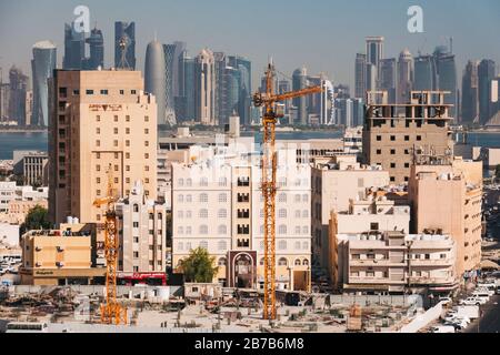 Ein Kran und Gebäude im Al Souq-Gebiet von Doha, mit der modernen Skyline des Finanzviertels, die im Hintergrund über die Bucht sichtbar ist Stockfoto