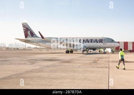 Bodenbesatzungen nehmen an einem Airbus A320 der Qatar Airways, wie er auf einem abgelegenen Stand am Hamad International Airport in Doha parkt, an