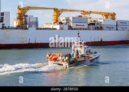 Ein kleines traditionelles Fischfang wird in den Schatten gestellt, wenn es an einem großen Containerschiff im Hafen von Portsmouth, Portsmouth, Hampshire, Südküste Englands vorbeikommt Stockfoto