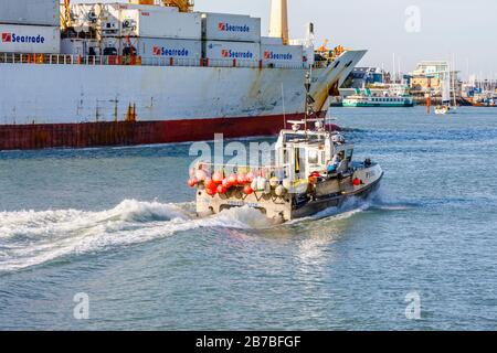 Ein kleines traditionelles Fischerboot wird von einem großen Containerschiff in der Nähe von Gosport im Portsmouth Harbour, Portsmouth, Hampshire, Südengland in den Schatten gestellt Stockfoto