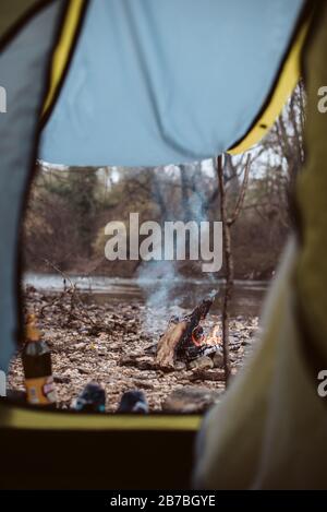 Feuer brennt in Brandgrube neben Zelt und Fluss auf Campingausflug Stockfoto