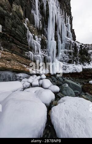 Gefrorene Seeps bilden Eiszapfen und Wasserfälle entlang der felsigen Klippen von Herring Cove, in der Nähe von Champneys West in Neufundland, Kanada Stockfoto