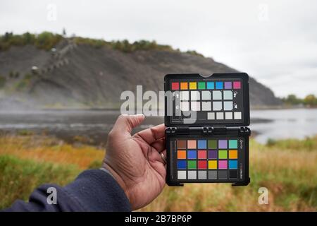 Frau, die den X-Rite Colorchecker Pass an Ort und Stelle hält, um den Weißabgleich der Kamera und ein Farbkalibrierungsfoto zu erhalten Stockfoto