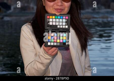 Frau, die den X-Rite Colorchecker Pass an Ort und Stelle hält, um den Weißabgleich der Kamera und ein Farbkalibrierungsfoto zu erhalten Stockfoto