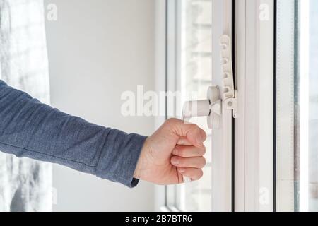 Weibliche Hand schloss ein modernes weißes PVC-Fenster mit einer Befestigungsvorrichtung für die Belüftung bei Tageslicht. Stockfoto
