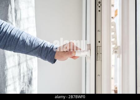 Die Hand öffnet ein PVC-Fenster, in dem der Griff in horizontaler Position gehalten wird, mit einer Befestigungsvorrichtung, die am Rahmen für die Belüftung befestigt ist. Stockfoto